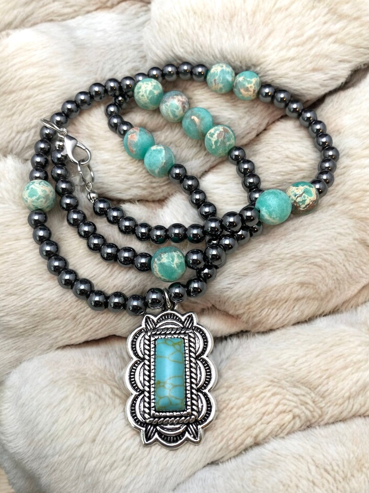 Necklace with gray beads and turquoise stones on a textured beige surface