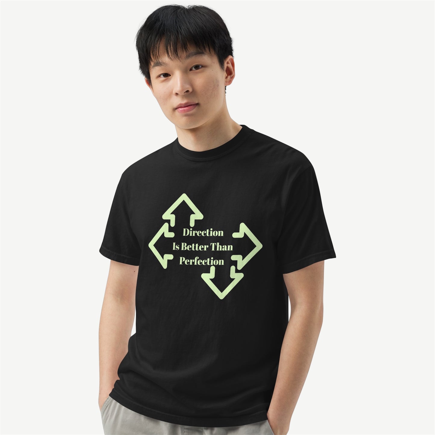 A young man wearing a black crewneck t-shirt with a light green graphic of four arrows pointing in different directions and the text 'Direction is Better Than Perfection' printed on the chest, set against a plain light gray background.