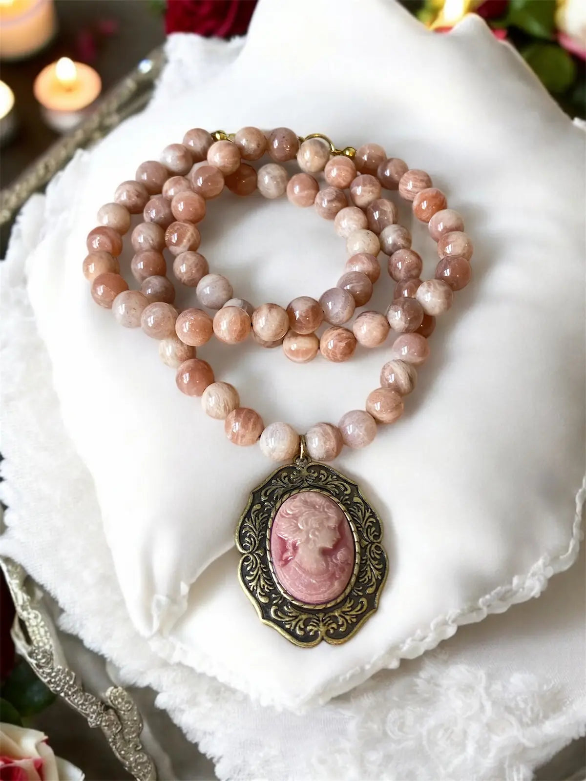 Necklace with pink beads and a cameo pendant on a white fabric background