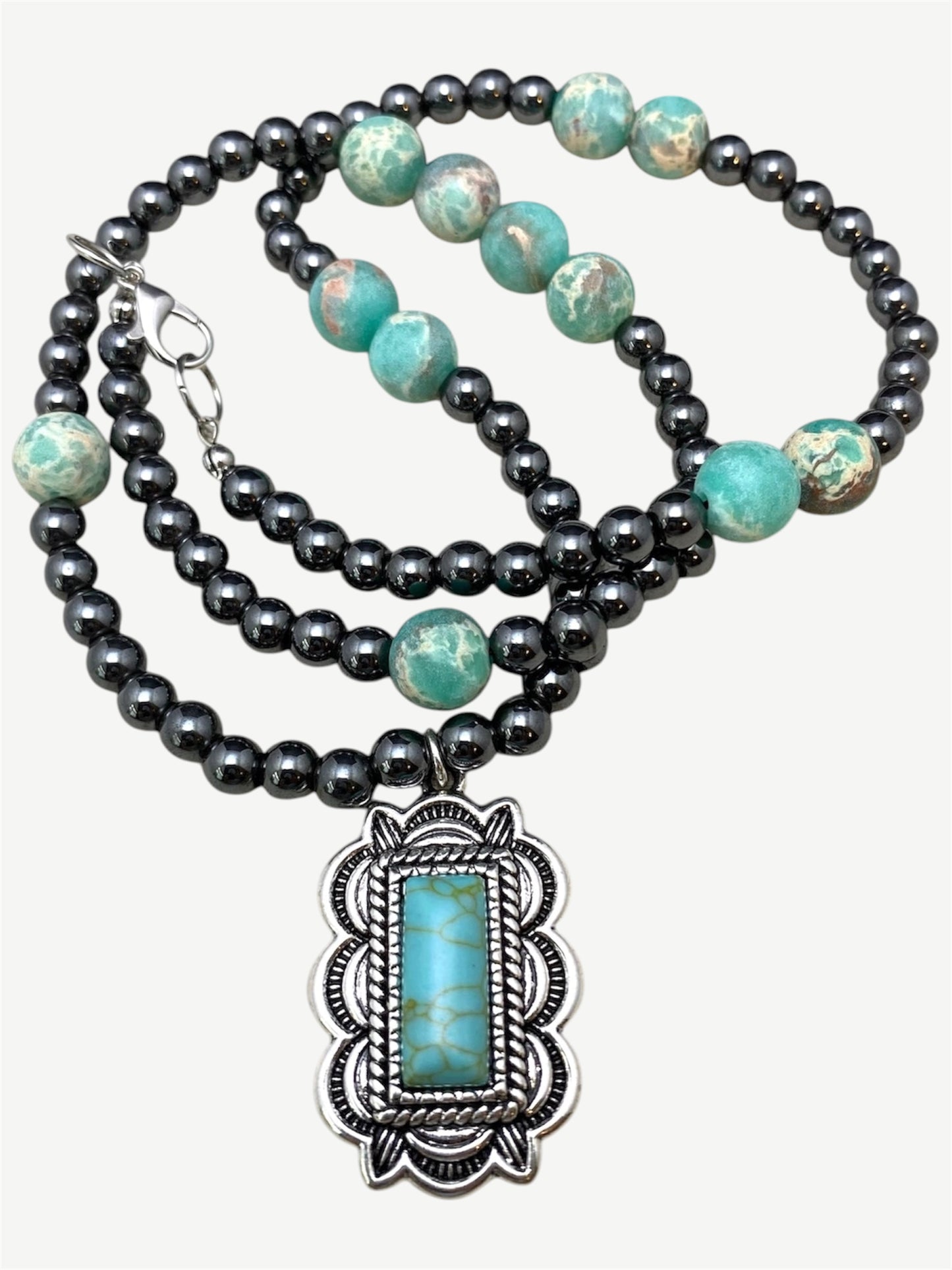 A bohemian-style double-strand necklace featuring dark gray beads and turquoise-colored beads, with a large silver-toned pendant containing a rectangular turquoise stone.