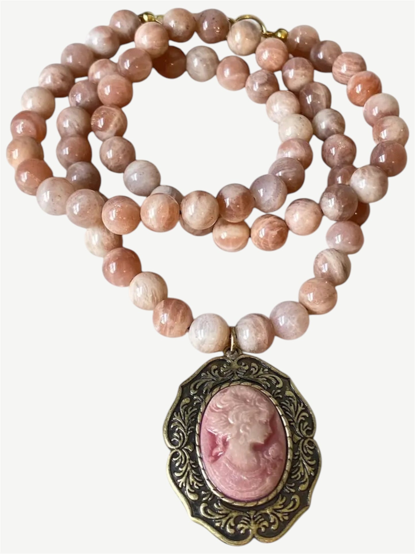 A beaded necklace featuring round, polished pink and peach stone beads, with a central oval pendant containing a carved pink classical profile set in an ornate antique bronze frame.