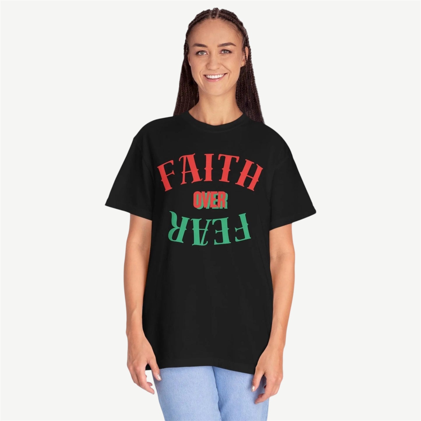 A woman modeling a black oversized graphic t-shirt with the text 'FAITH OVER FEAR' printed on the front in red and green, paired with light blue jeans against a light gray background.