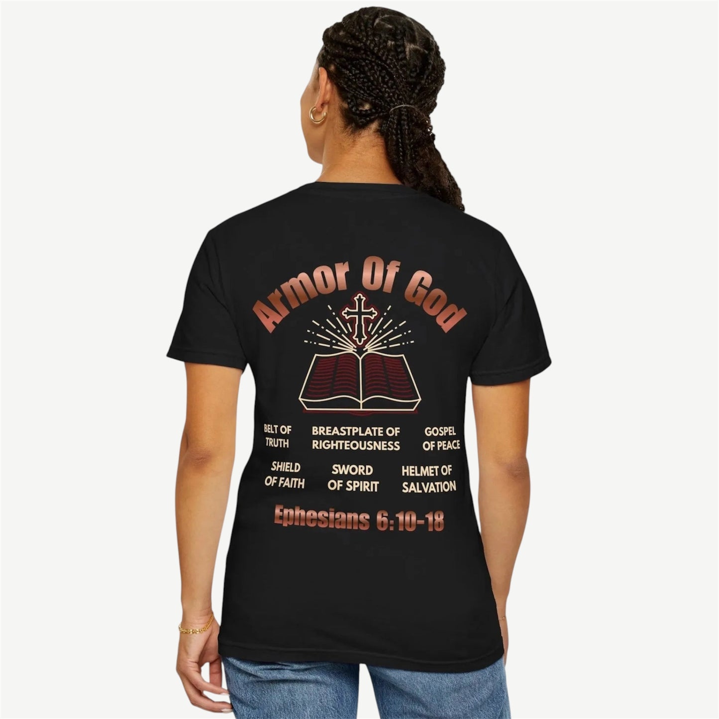 A woman shown from the back wearing a black t-shirt with a large graphic print on the back. The graphic features the text 'Armor Of God' in a reddish-brown font above an illustration of an open Bible with a cross, followed by theological terms and the scripture 'Ephesians 6:10-18' at the bottom.
