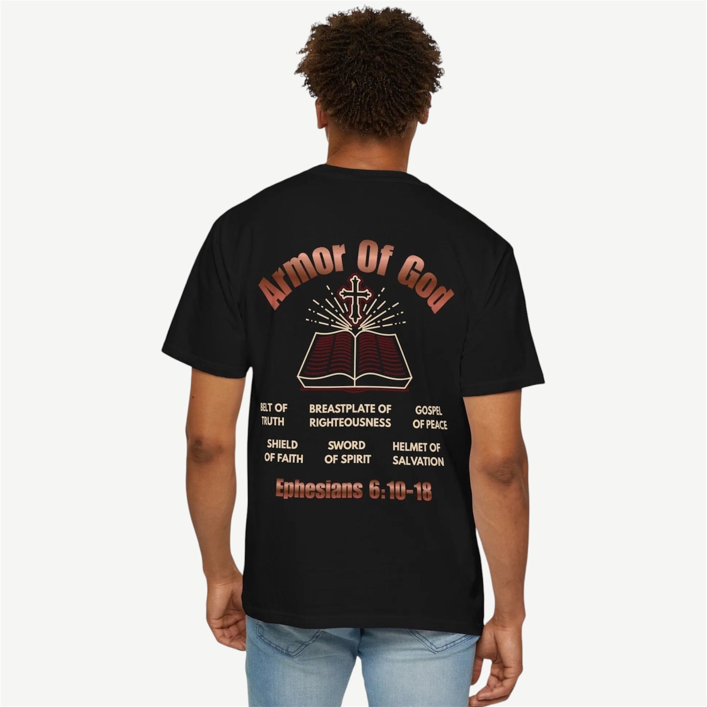 A man viewed from behind wearing a black t-shirt with a large graphic print on the back. The graphic features the text 'Armor Of God' in a reddish-brown font above an illustration of an open Bible with a cross on top, surrounded by various biblical phrases and 'Ephesians 6:10-18' at the bottom.